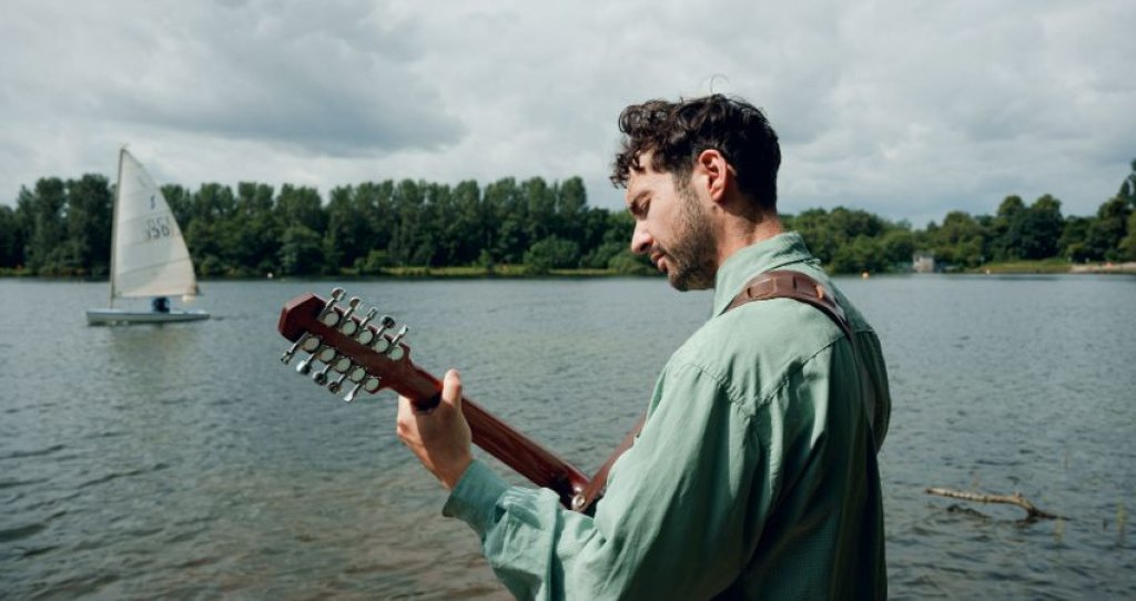 Séamus Óg playing guitar in front of a lake.
