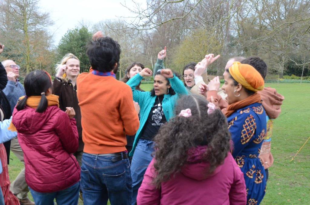 Photo by Morwan Osman shows a group of colourfully dressed people dancing in a big group in a park.