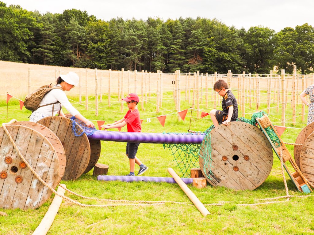 Three children playing imaginatively with barrels, nets and tubes.